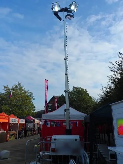 Lighting tower with its mast raised beside stalls at an outdoor show